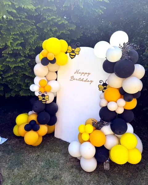 Yellow, black and white bumblebee-themed balloon arch backdrop for a birthday party