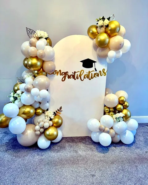 Gold and cream balloon arch backdrop with "Congratulations" signage for a graduation celebration