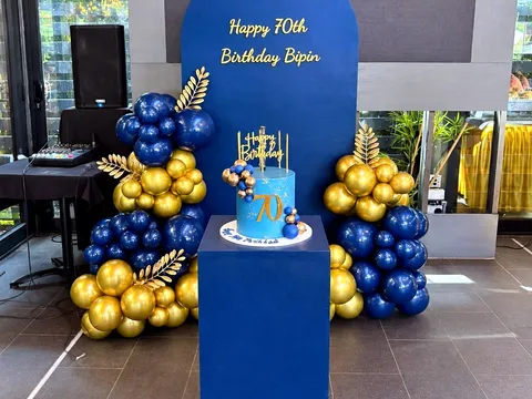 Navy plinth displaying a birthday cake, styled alongside a matching balloon backdrop