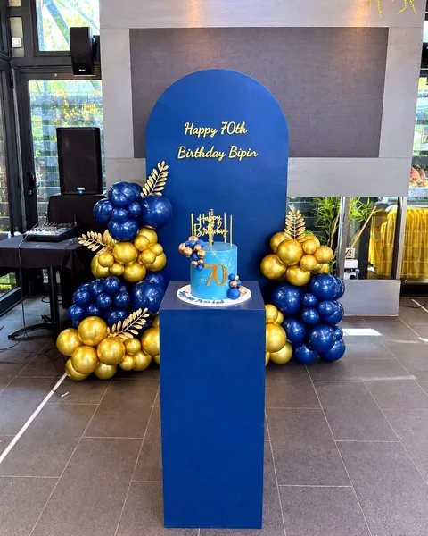 Navy and gold balloon backdrop with a birthday cake on a plinth, styled for a 70th birthday celebration